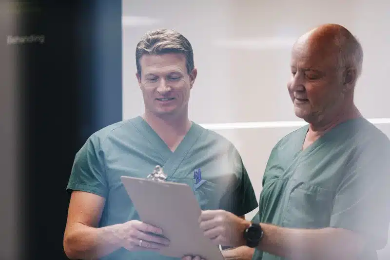 Bilde av Dr. Jo Andreas Ording og Dr. Jørn Bremnes som holder et clipboard og diskuterer innholdet på dokumentet de leser - Stamcelleklinikken - Artrose