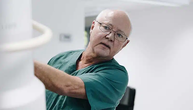 Bilde av Dr. Jørn Bremnes som står inne på et behandlingsrom på klinikken og justerer en maskin - Stamcelleklinikken - Artrose